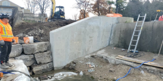 Stone wall and concrete retaining wall with construction equipment and workers