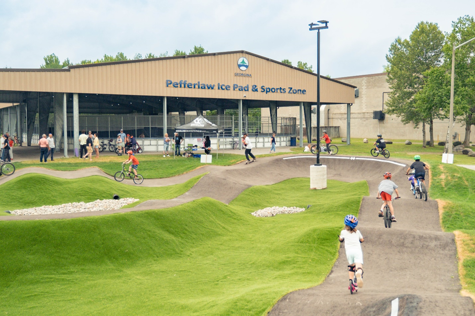 concrete pump track with several children on bikes and scooters