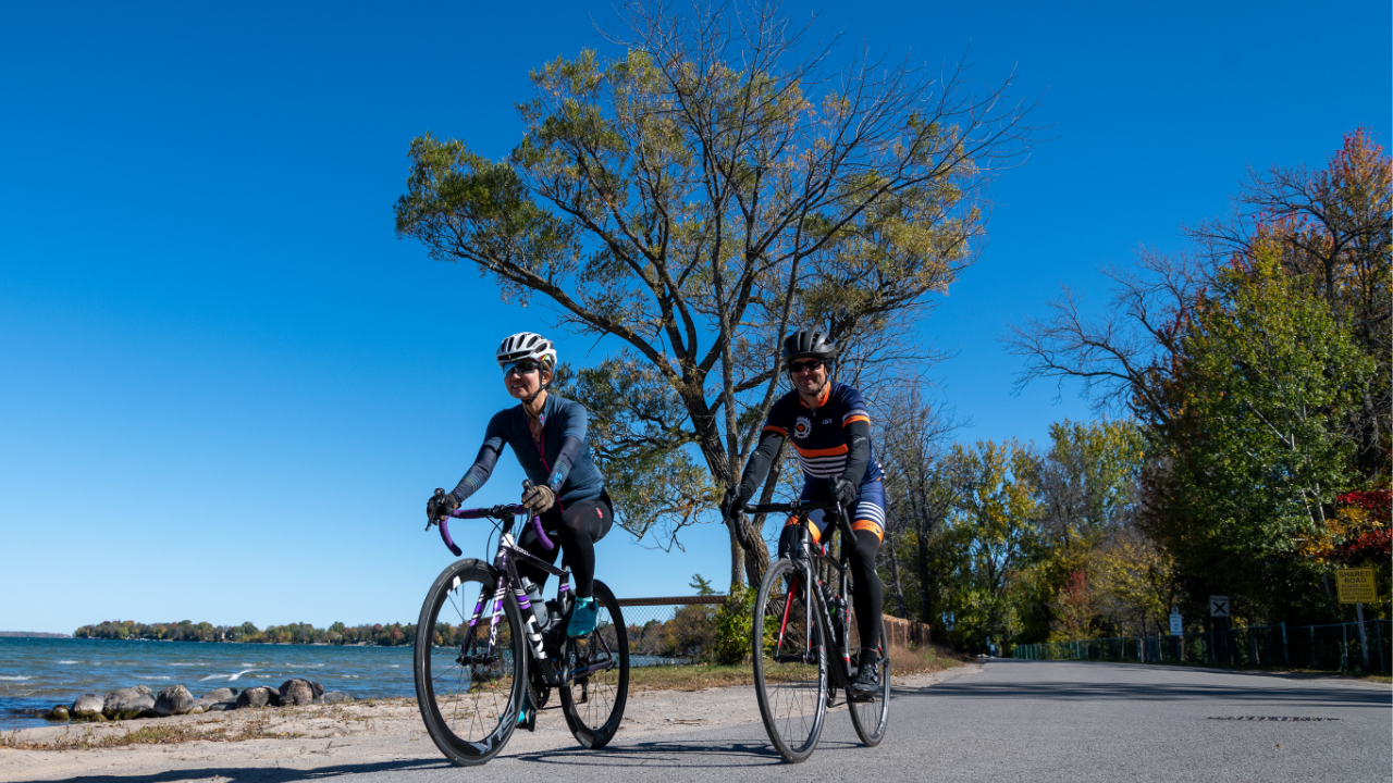 two adults riding bicycles on a road by a lake