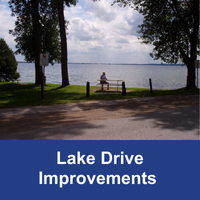 Solitary individual sitting on a bench on the side of a lake with blue bar and text Lake Drive Improvements