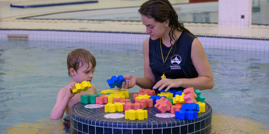 trainer and child playing with blocks in the water of a public pool