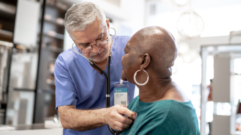 man in scrubs using stethoscope on older female