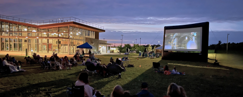 People sitting outside the ROC chalet watching a movie at night 