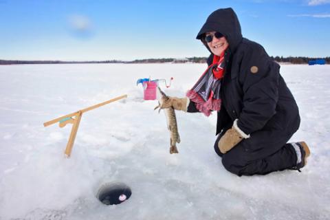 Woman smiling and holding a just-caught fish over fishing hole in Lake Simcoe