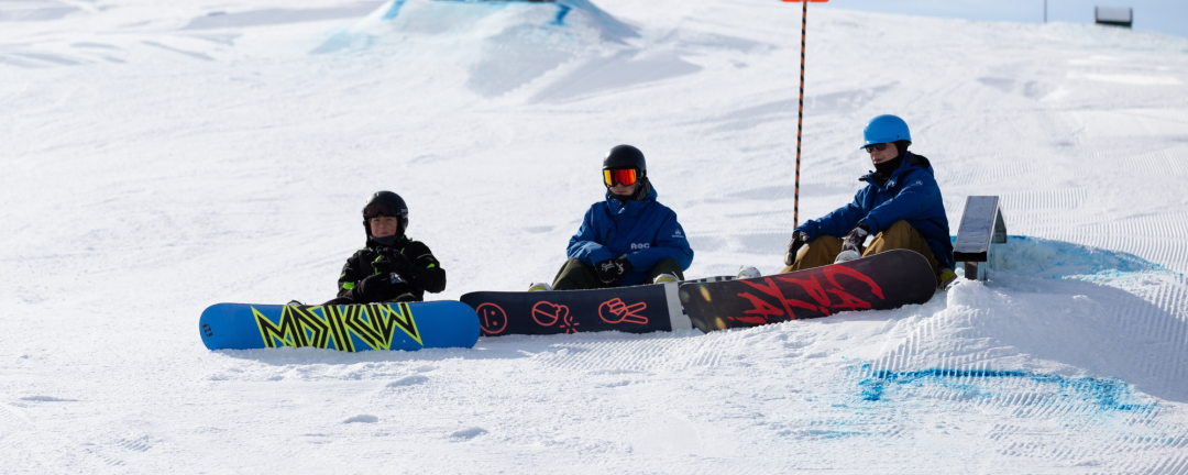 three people sitting in the snow with snowboards